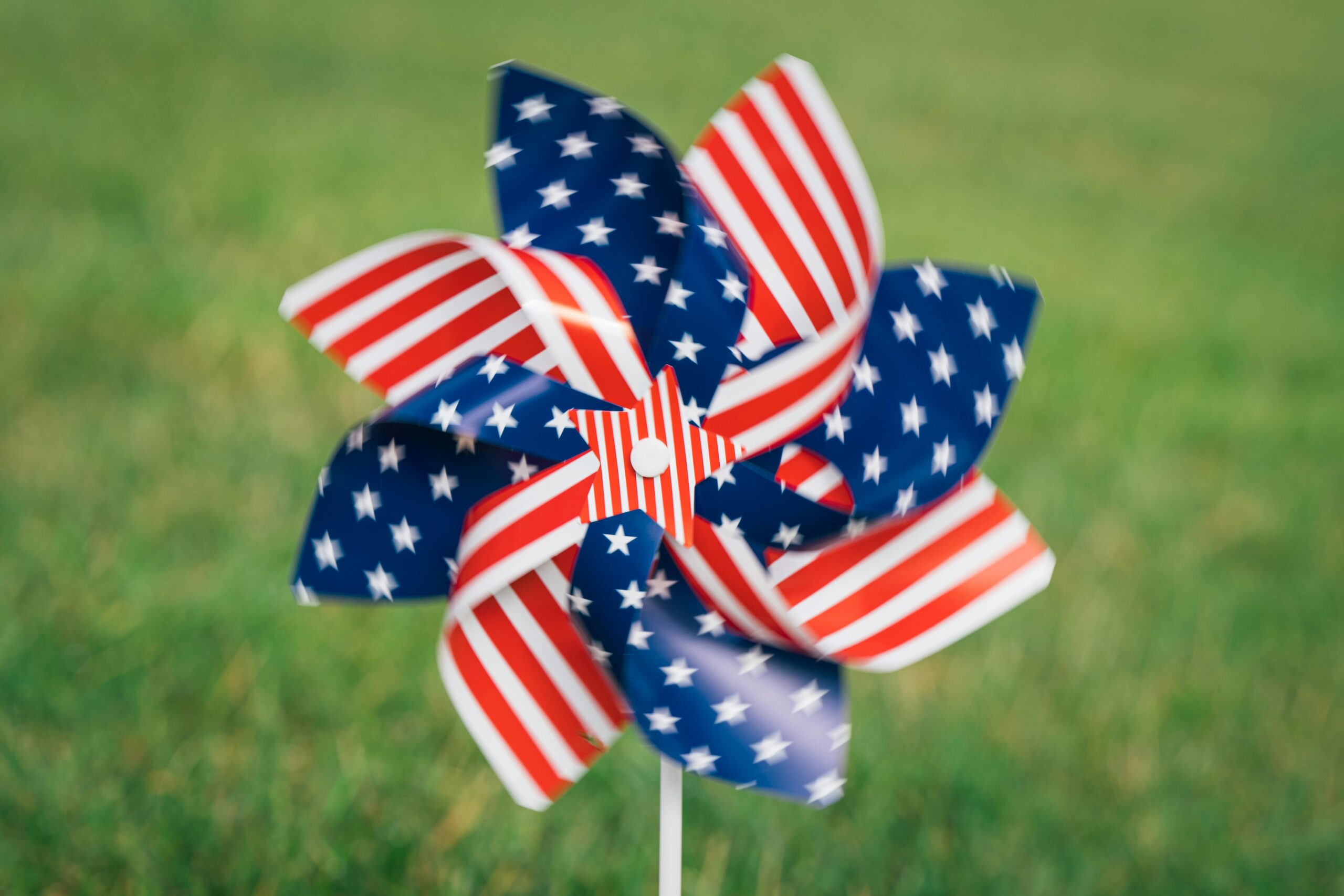 Blurred American flag-themed pinwheel spinning outdoors on grass, symbolizing patriotism.